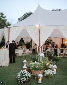 a group of people standing under a tent next to tables and chairs with flowers on them