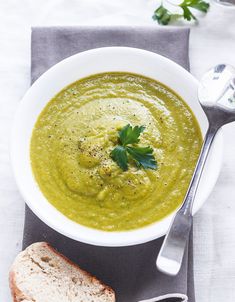 a white bowl filled with green soup next to a slice of bread on a napkin