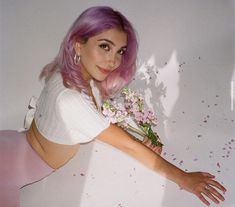 a woman with pink hair and flowers in her hand is leaning against a wall, posing for the camera