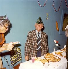 an old man wearing a party hat standing next to two older women at a table