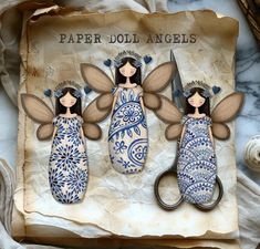 paper doll angels are holding scissors on top of a piece of parchment with blue and white designs