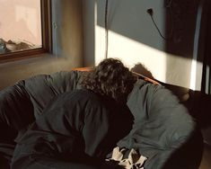 a man laying on top of a black couch next to a window