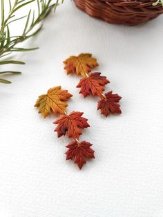 three pairs of earrings with leaves on them sitting next to a basket and pine branch