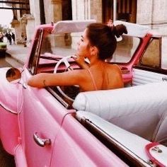 a woman sitting in the driver's seat of a pink car