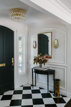 a black and white checkered floor in a room with a table, mirror and vase