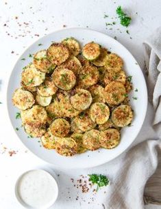 a white plate topped with fried zucchini next to a bowl of ranch dressing