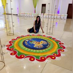 a woman is sitting on the floor in front of a colorful rangolite design