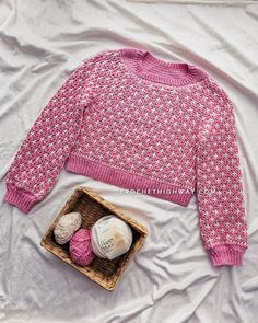 a pink sweater and two balls of yarn in a basket on top of a bed