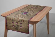 a wooden table topped with a brown and pink table runner next to a white wall