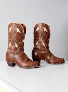 This is a pair of vintage cowboy boots circa 1950. The saddle brown western "Pee Wee" boots feature a white inlay leather design. They have a high wood stacked heels with metal taps and cloth pulls.  CONDITION In good condition with wear consistent with age and use. Scuffs and patina to the leather. One of the pulls stitching is loose, and there is a tiny break in the center front of the top edge on the left boot.  APPROXIMATE FIT: Women's 6.5 MEASUREMENTS Approximate Insole:  9.5"  ...  24.1 cm Cowboy Boots Brown, Leather Inlay, Vintage Cowboy Boots, Pee Wee, Vintage Cowboy, Saddle Brown, Cowboy Western, Western Cowboy Boots, Boots Brown