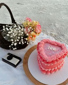 a heart shaped cake sitting on top of a table next to a basket filled with flowers