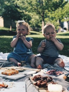 two children sitting on a blanket eating food