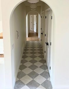 an arched hallway leading to another room with white walls and checkered tile flooring