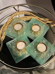 four candles are sitting on top of some glass blocks with pearls around them and beads hanging from the sides