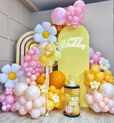 a birthday party with balloons and flowers on the wall, near a sign that says happy birthday