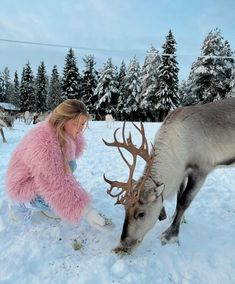 a woman kneeling down next to a reindeer in the snow with it's nose on something