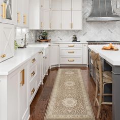 a kitchen with white cabinets and wood floors, an area rug on the floor in front of the stove