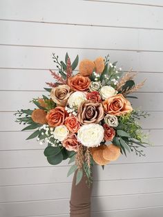 a bouquet of flowers in a vase against a white wall with brown and orange accents