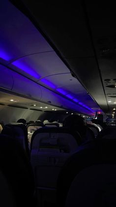 the inside of an airplane with blue lights on it's ceiling and seats down