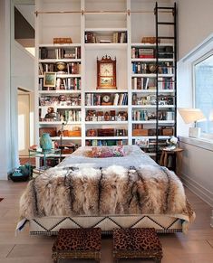 a bedroom with bookshelves filled with lots of books and fur on the bed