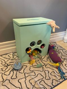 a toy storage box with toys in it on the floor next to a stuffed animal