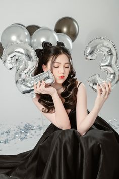 a woman in a black dress is holding some silver balloons