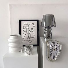 a white table topped with two vases next to a wall mounted clock and lamp