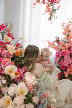 a woman holding a baby in her arms surrounded by pink and orange flowers on display