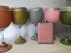 there are many different colored wine glasses on the table with silver and pink flasks