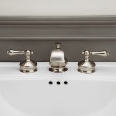 three silver faucets sitting on top of a white sink