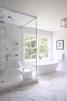 a large white bathroom with marble flooring and glass shower doors, windows, and a freestanding tub