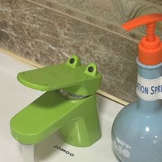 a green frog soap dispenser sitting on top of a bathroom sink next to a bottle