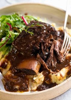 a bowl filled with meat and potatoes covered in gravy next to a salad