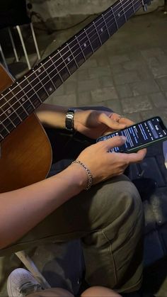 a person sitting on the ground with a cell phone in their hand and a guitar next to them