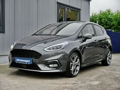 a black ford monde is parked in front of a building with two cars behind it