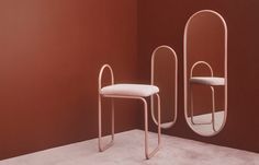 two white chairs sitting next to each other in front of a red wall with an oval mirror