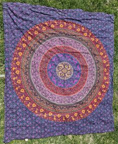 a purple and red circular quilt on the grass