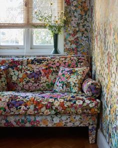 a floral couch sitting in front of a window next to a vase with flowers on it