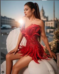 a woman in a red feathered dress sitting on top of a white ballon