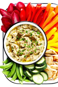 a bowl of dip surrounded by sliced vegetables and pita bread on a platter