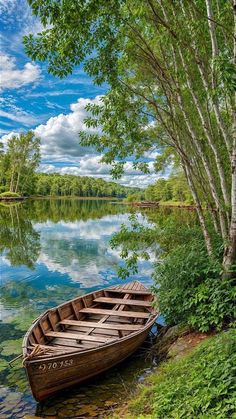 a boat sitting on the shore of a lake next to some trees and water with clouds in the sky