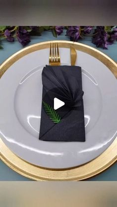 a white plate topped with a black napkin next to a gold fork and purple flowers