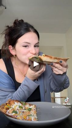 a woman eating a slice of pizza on top of a plate in front of her