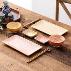 a wooden table topped with plates and bowls next to vases on top of it