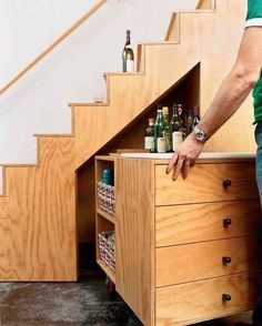 a man standing in front of a wooden drawer under stairs with beer bottles on it