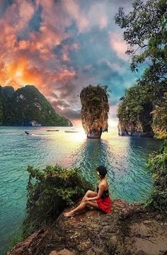 a woman sitting on top of a rock next to the ocean under a cloudy sky