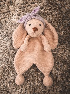 a crocheted pink teddy bear laying on top of a pile of brown carpet