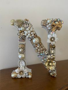 the letter n is made out of pearls and other beads on a wooden table with a white wall in the background