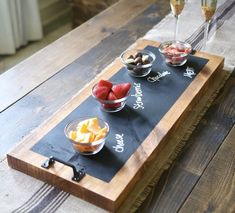 a wooden table topped with bowls and cups filled with fruit on top of a blackboard