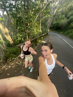 a woman taking a selfie with her friend on the road in front of some trees